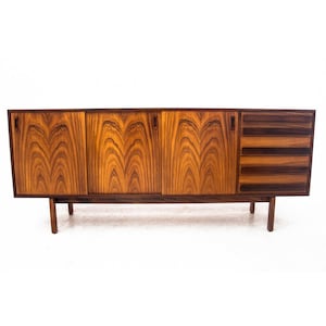 Peut inclure: Un buffet moderne du milieu du si&egrave;cle avec trois portes et quatre tiroirs. Le buffet est en bois fonc&eacute; avec un riche motif de grain. Il a un design simple avec des lignes droites et une forme rectangulaire.