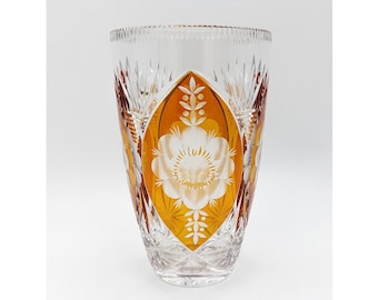 May include: A clear crystal vase with an amber-colored floral design. The vase features a cut-glass pattern and a central oval panel with a white flower motif. The vase is approximately 8 inches tall.