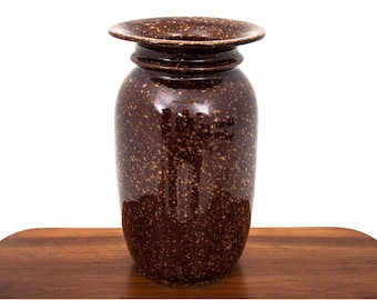 May include: A brown ceramic vase with a speckled glaze. The vase has a wide, flared opening and a narrow neck.