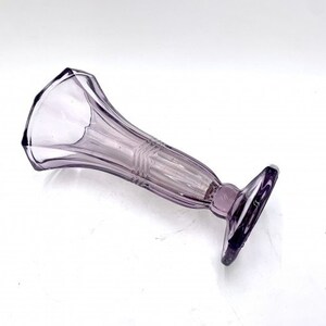 May include: A purple glass bud vase with a geometric design. The vase has a wide mouth and a narrow base.