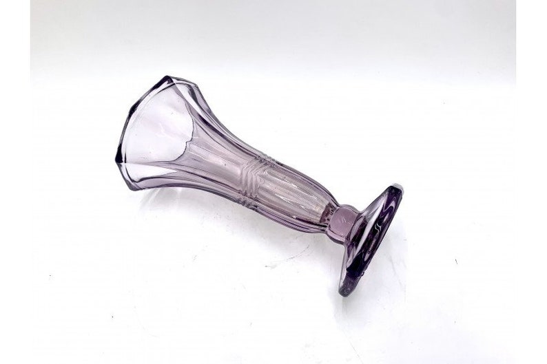 May include: A purple glass bud vase with a geometric design. The vase has a wide mouth and a narrow base.