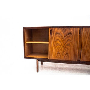 Peut inclure: Un buffet moderne du milieu du si&egrave;cle avec des portes coulissantes en bois fonc&eacute; avec un riche motif de grain. Le buffet a une seule &eacute;tag&egrave;re ouverte et repose sur quatre pieds.