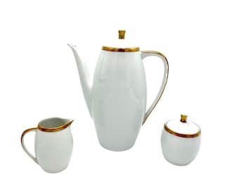 May include: A white porcelain coffee pot, creamer, and sugar bowl set with gold trim. The set is perfect for serving coffee and tea.