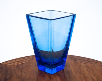 May include: A blue glass vase with a square shape and a geometric design. The vase is sitting on a wooden table.