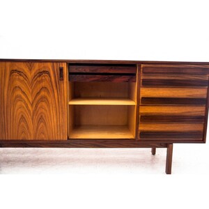 Peut inclure: Un buffet moderne du milieu du si&egrave;cle avec une finition en bois vein&eacute;. Le buffet comporte deux tiroirs, une &eacute;tag&egrave;re et une porte. La porte est ouverte, r&eacute;v&eacute;lant l'&eacute;tag&egrave;re &agrave; l'int&eacute;rieur. Le buffet est en bois et a une finition brun fonc&eacute;.