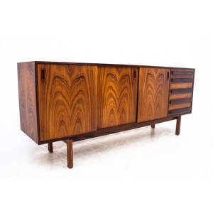 Peut inclure: Un buffet moderne du milieu du si&egrave;cle avec trois portes coulissantes et quatre tiroirs. Le buffet est en bois fonc&eacute; avec un beau grain. Il a une forme rectangulaire et repose sur quatre pieds.