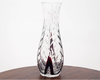 May include: A clear glass vase with a cut glass design. The vase has a wide mouth and a narrow base. The vase is decorated with a black and red stripe.