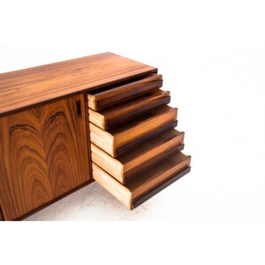 Peut inclure: Un buffet moderne du milieu du si&egrave;cle avec cinq tiroirs et une porte de placard. Les tiroirs sont ouverts et faits de bois avec une finition brun fonc&eacute;. La porte du placard est ferm&eacute;e et pr&eacute;sente un motif de grain de bois.