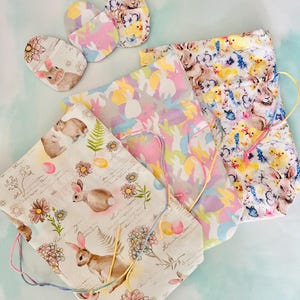 May include: A selection of Easter-themed fabric items. The collection includes drawstring bags and coasters, all decorated with pastel colours and spring-themed patterns. Designs feature bunnies, chicks, eggs, and floral elements.