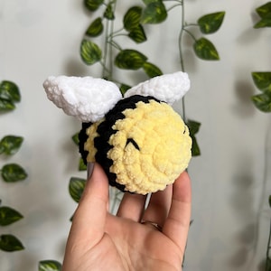 May include: A crocheted bee plush toy with white wings, a black and yellow striped body, and a smiling face.