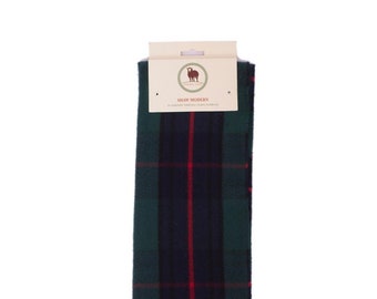 Op de afbeelding: Een groene, blauwe en rode geruite sjaal met franjes. De sjaal heeft een label met de tekst "Shaw Modern" en "Pure New Zealand Wool Scarf".