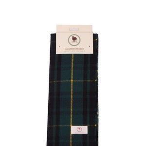 Op de afbeelding: Een groene, zwarte en gele geruite sjaal met franjes. De sjaal heeft een label met de tekst "MacArthur Modern" en "Pure Soft Tartan Clan Scarf".