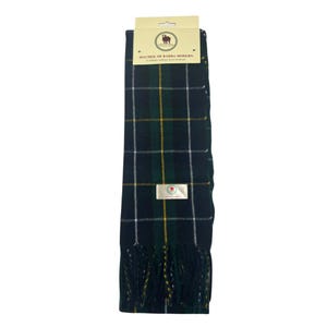 May include: A green, white, and yellow plaid scarf with fringe. The scarf has a label that reads "Macneil of Barra Modern" and a small sheep logo.
