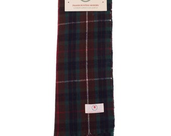 May include: A Fraser Hunting Modern tartan scarf in shades of green, burgundy, and white. The scarf has a fringed edge and a tag with the brand name and logo. The scarf is approximately 60 inches long.