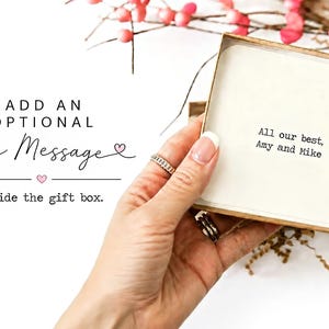 May include: A square cardboard gift box containing a white card with the printed text: All our best, Amy and Mike. To the left, the text reads: ADD AN OPTIONAL Free Message inside the gift box, with small pink heart icons.