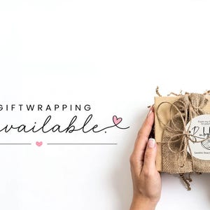 May include: A square cardboard gift box wrapped in brown burlap fabric with twine, featuring a circular white label with the text RubyJune and a citrus slice graphic. The text GIFTWRAPPING is available is printed in black with pink hearts.