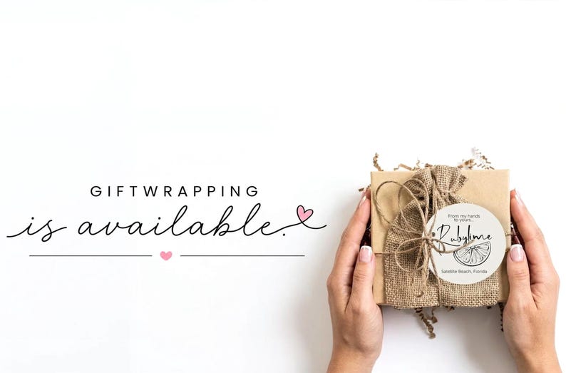 May include: A square cardboard gift box wrapped in brown burlap fabric with twine, featuring a circular white label with the text RubyJune and a citrus slice graphic. The text GIFTWRAPPING is available is printed in black with pink hearts.