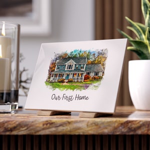 May include: A rectangular white ceramic tile display featuring a watercolor-style illustration of a two-story house with a front porch, green lawn, and trees. The text "Our First Home" is printed in black script below the house illustration.