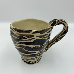 May include: A ceramic mug with a black and white striped pattern. The mug has a rounded body and a handle.