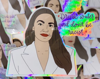 May include: A holographic sticker featuring a cartoon illustration of a woman with brown hair and a white blazer. The sticker has the text "Drink water and don't be racist" with a star on each side of the text. The text is in purple and the background is a rainbow holographic effect.