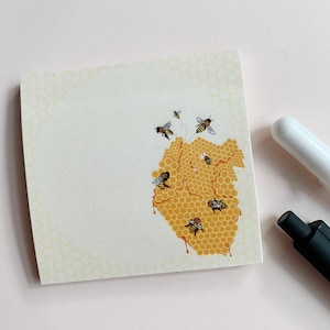 May include: A yellow and white sticky note with a honeycomb design and bees flying around a honeycomb. The bees are black and yellow.