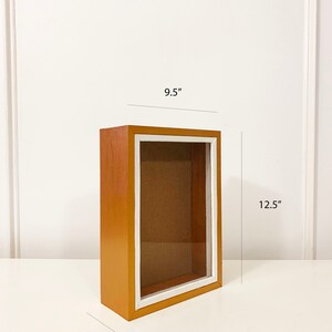 May include: A wooden picture frame with a white inner border. The frame is 9.5 inches wide, 12.5 inches tall, and 3.5 inches deep.