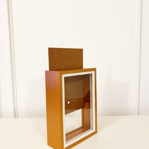 May include: A wooden shadow box with a white frame and a clear glass front. The box is empty and has a small hole in the back.