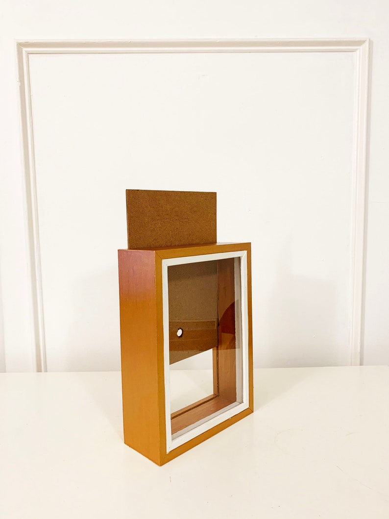 May include: A wooden shadow box with a white frame and a clear glass front. The box is empty and has a small hole in the back.
