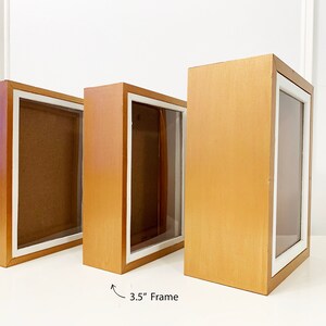 May include: Three wooden shadow boxes with white matting and clear glass fronts. The boxes are 3.5 inches wide and are arranged in a row from smallest to largest.