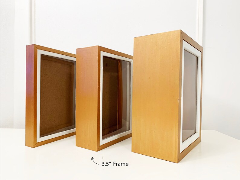 May include: Three wooden shadow boxes with white matting and clear glass fronts. The boxes are 3.5 inches wide and are arranged in a row from smallest to largest.