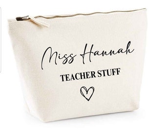 May include: A cream-colored canvas cosmetic bag with a gold zipper. The bag features the text "Miss Hannah" in a cursive font, "TEACHER STUFF" in a block font, and a heart symbol. The bag is designed for teachers.
