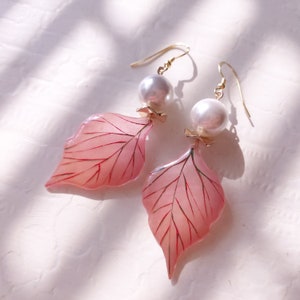 May include: A pair of pink leaf-shaped earrings with gold accents and white pearl drops.