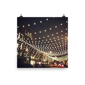 May include: A city street at night with string lights strung across the street. The lights are blurred and create a festive atmosphere.
