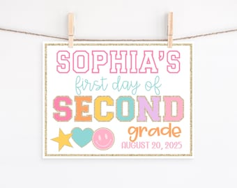 May include: A colorful sign with the text "SOPHIA'S first day of SECOND grade" in pink, blue, orange, and purple. The sign includes a star, heart, and smiley face graphic, and the date "AUGUST 20, 2025". The sign is held by two wooden clips.