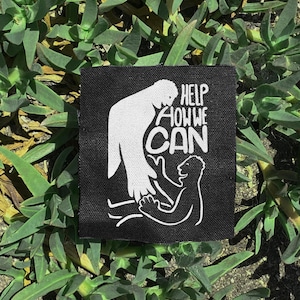 Puede incluir: Un parche cuadrado negro con arte gráfico y texto en blanco. El arte representa a una persona ayudando a otra. El texto dice "HELP HOW WE CAN". El parche está sobre un fondo de plantas verdes.