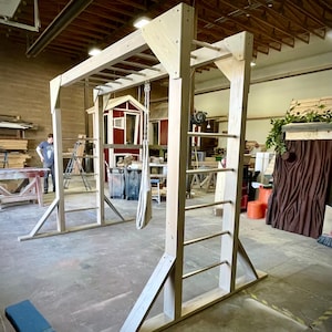 May include: A wooden climbing frame with a ladder and monkey bars. The frame is made of natural wood and has a rustic look. It is set up in a workshop setting.