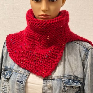 Könnte beinhalten: Ein leuchtend roter Strickschal mit gelben, blauen und grünen Sprenkeln. Der handgefertigte Schal wird auf einer Schaufensterpuppe mit einer Jeansjacke präsentiert. Dieser kuschelige Halswärmer ist ein stilvolles Accessoire.