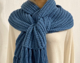 May include: A blue knitted scarf with long fringe tassels. The scarf is folded and draped around a mannequin's neck.