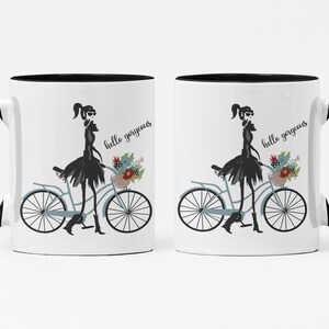 May include: Two white coffee mugs with black rims and handles. Each mug features a black silhouette of a woman riding a bicycle with flowers in the basket. The text "hello gorgeous" is printed on each mug.
