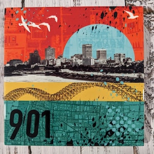 May include: Square art print featuring a Memphis skyline, bridge, and map elements. The design incorporates a red and blue sky, a yellow bridge, and a teal map with the number "901". White birds fly across the top. Black paint splatters add a modern touch.