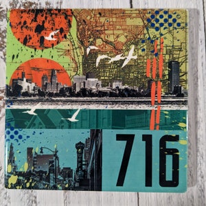 May include: A colorful square tile with a cityscape and a map design. The tile has a blue, green, and yellow background with red and white accents. The tile also features the number 716.