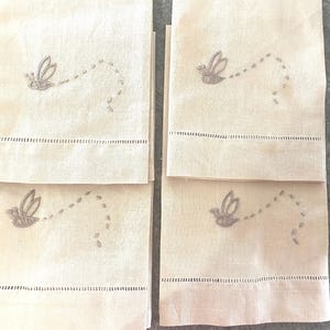Pode incluir: Conjunto de quatro toalhas de chá de linho branco com pássaros voadores bordados e trilhas pontilhadas.