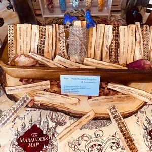 May include: A wooden bowl filled with Palo Santo sticks, each engraved with words like "Inspiration" and "Clarity." Dried flowers and a small burlap sack are nestled among the sticks. The display sits on a map-themed surface.