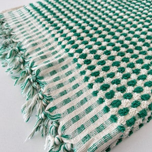 May include: A green and white checkered bath towel with a textured surface. The towel has a fringe border.