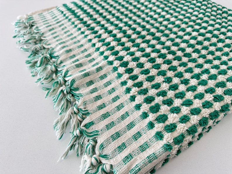 May include: A green and white checkered bath towel with a textured surface. The towel has a fringe border.