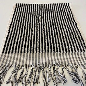 May include: Black and white striped bath towel with fringe trim. The towel is made of a soft, absorbent material and is perfect for drying off after a shower or bath.