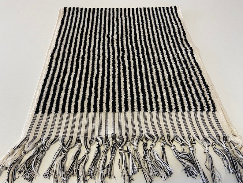 May include: Black and white striped bath towel with fringe trim. The towel is made of a soft, absorbent material and is perfect for drying off after a shower or bath.