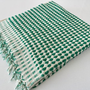 May include: A green and white checkered bath towel with a fringed edge. The towel is made of a soft, absorbent material.