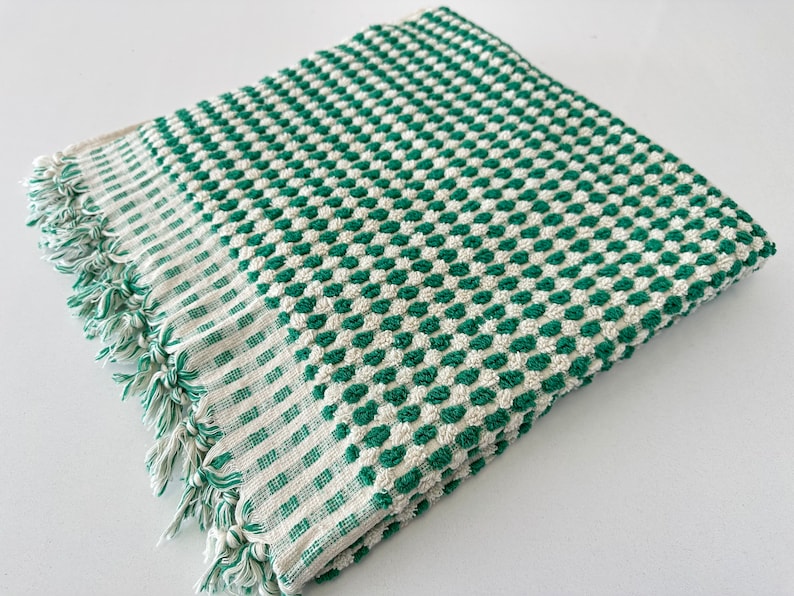 May include: A green and white checkered bath towel with a fringed edge. The towel is made of a soft, absorbent material.