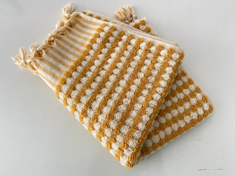 May include: Two yellow and white striped towels with a textured pattern of small circles. The towels are folded and have fringe on the ends.